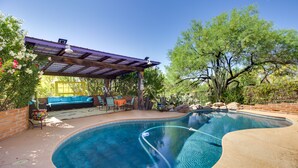Ein Pool mit geschwungener Kante, ein überdachter Sitzbereich mit Tisch und Stühlen sowie eine Pergola.