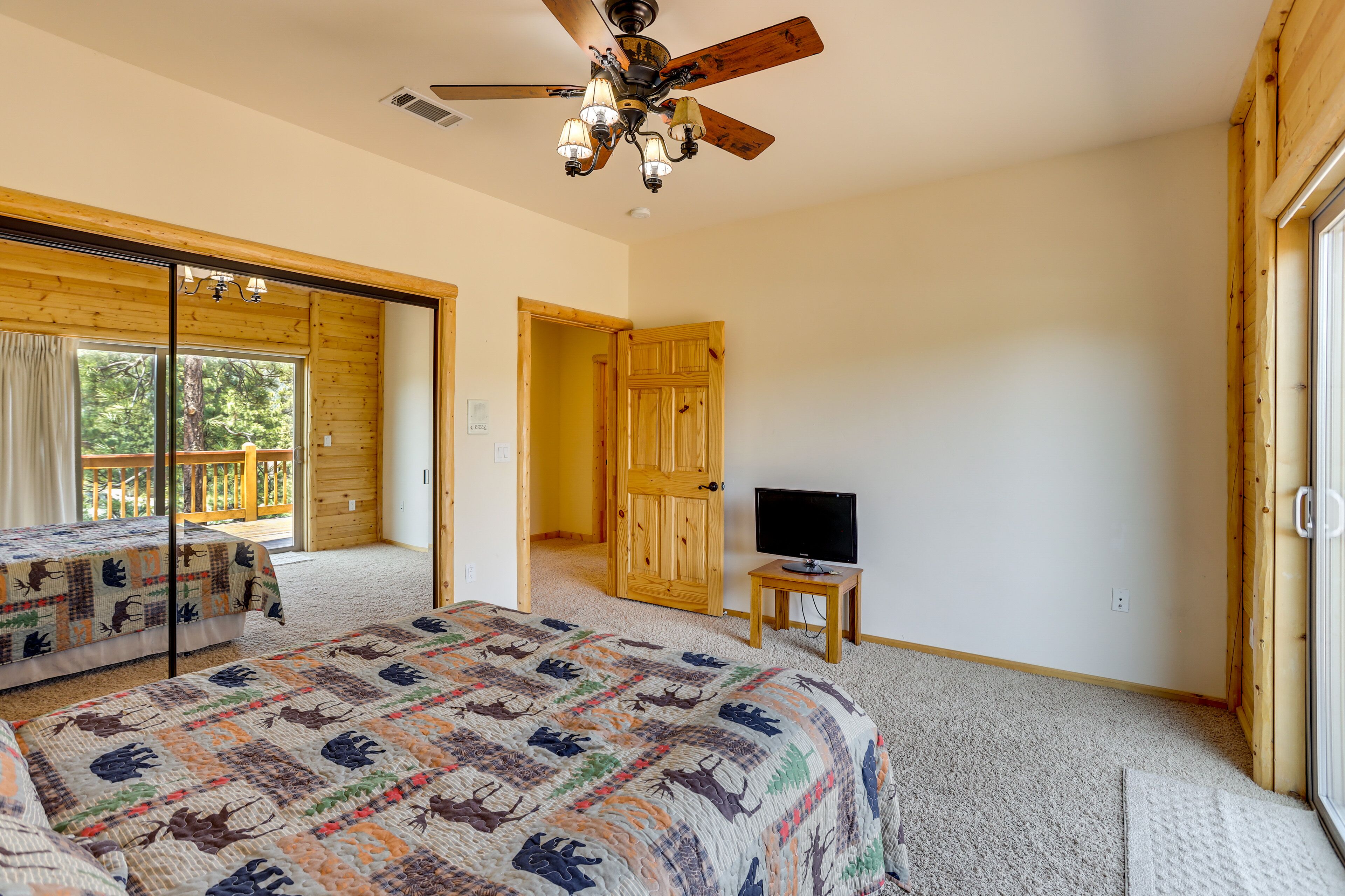 A bedroom with a large bed, a ceiling fan, a television on a small table, and a sliding glass door leading to a balcony.