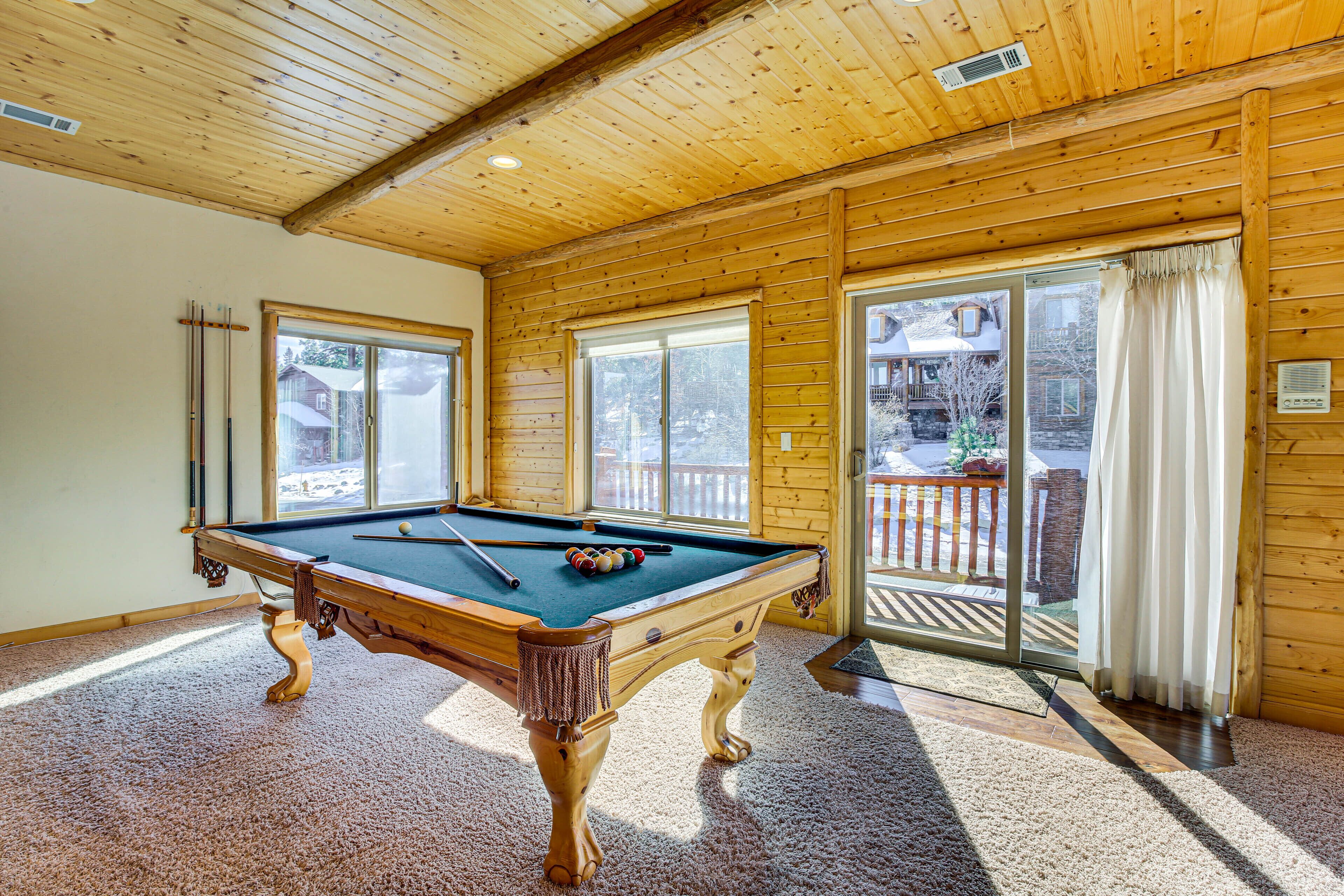 A pool table in a room with wooden walls and large windows.