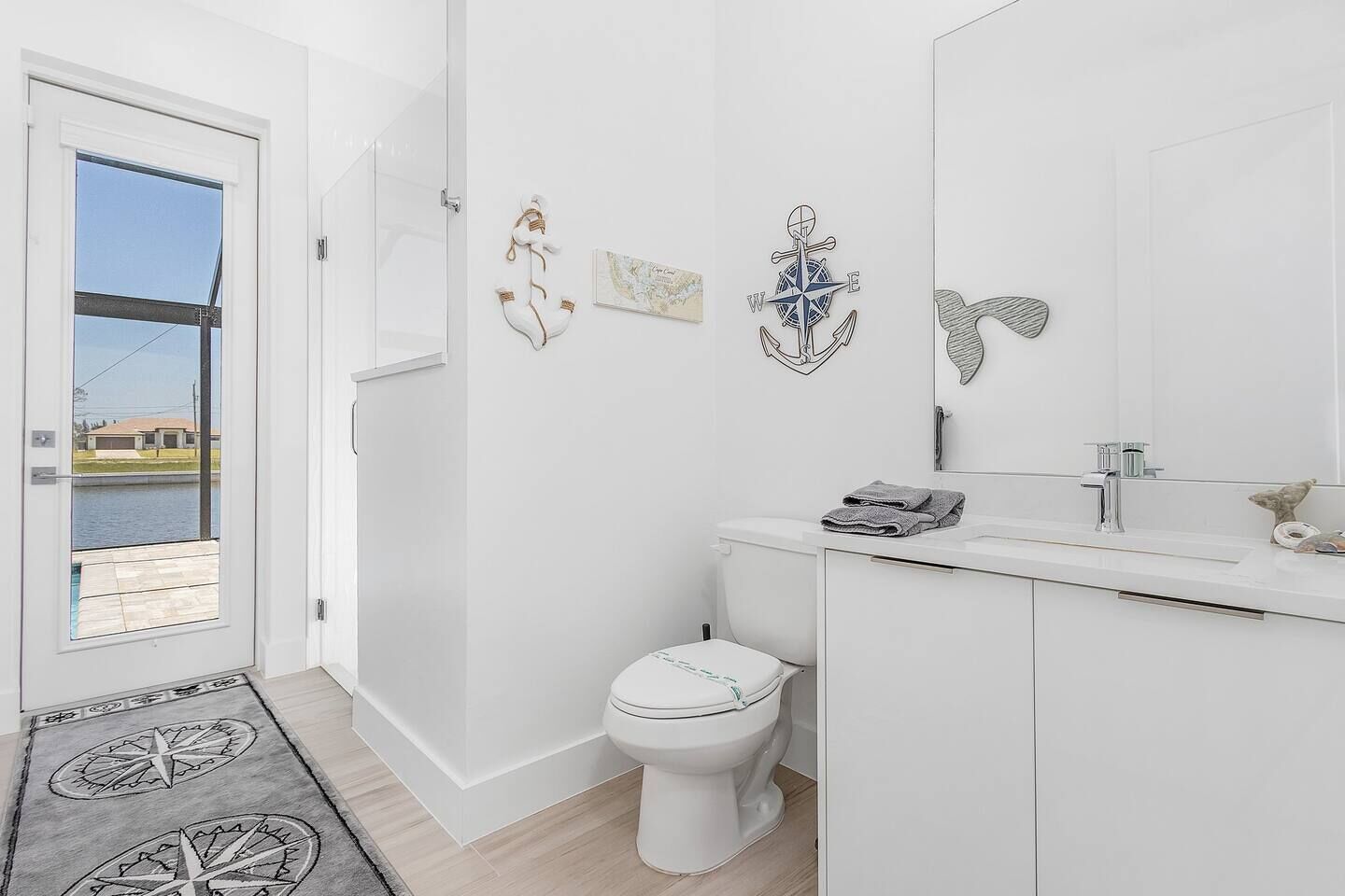 A modern bathroom with a toilet, sink, and a large mirror. There are decorative wall art pieces and a rug with a compass design.