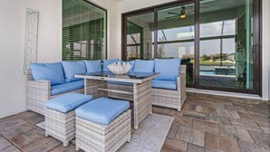 A patio area with wicker furniture, a glass table, and a view of a swimming pool.