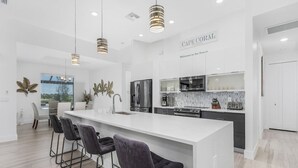 A modern kitchen with a large island, bar stools, stainless steel appliances, and a view of the outdoors.