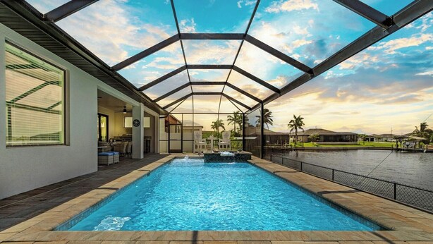 A swimming pool with a glass ceiling, surrounded by a patio area with chairs and a view of the water.
