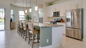 Een moderne keuken met een centraal eiland, roestvrijstalen apparatuur en een eethoek met barkrukken.