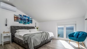 Un dormitorio con una cama, una mesita de noche, un sillón azul y un amplio ventanal con vistas.