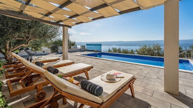 Un área junto a la piscina con tumbonas de madera, una piscina y vista al mar.