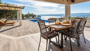 Un espacio exterior techado con piscina, mesa y sillas, con vista a un paisaje pintoresco.