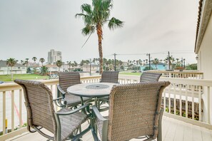 Ein Balkon mit Korbstühlen und einem Tisch, mit Blick auf ein Wohngebiet mit Palmen und Gebäuden.