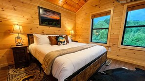 Une chambre à coucher dans une cabane en bois, avec un lit, deux lampes de chevet, un tapis et une grande fenêtre donnant sur la forêt.