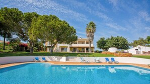 Une piscine avec des chaises longues, un grand arbre et un bâtiment à la façade jaune.