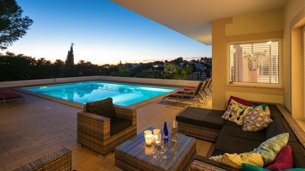 Un espace aménagé au bord de la piscine, avec des meubles en osier, une table basse en verre et une vue sur la piscine.