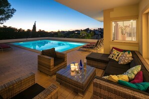 A poolside area with wicker furniture, a glass coffee table, and a view of the pool.
