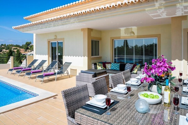 A poolside area with lounge chairs, a dining table set for two, and a flower arrangement.