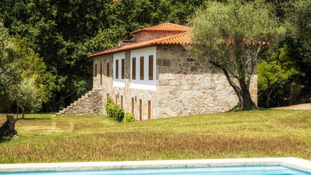Edificio de piedra con techo de tejas, rodeado de árboles y una piscina.