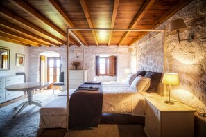 A bedroom with a four-poster bed, a bedside table with a lamp, a small desk with a chair, and a stone wall. - Villa Enia - Five Bedroom Villa, Sleeps 10 (Refóios do Lima)