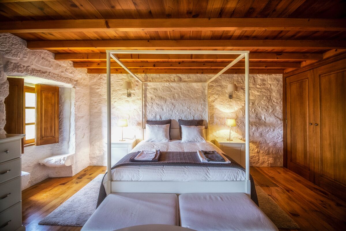Ein Schlafzimmer mit Himmelbett, Steinwänden, Holzbalken und einem Schrank aus Holz.