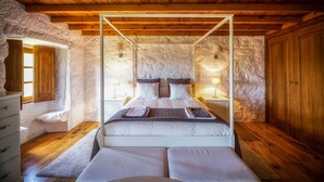 Un dormitorio con cama con dosel, paredes de piedra, vigas de madera y un armario de madera.