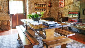 A stone-walled room with a wooden table, benches, and a patterned rug. - Villa Estora - One Bedroom Villa, Sleeps 2 (Estorãos)