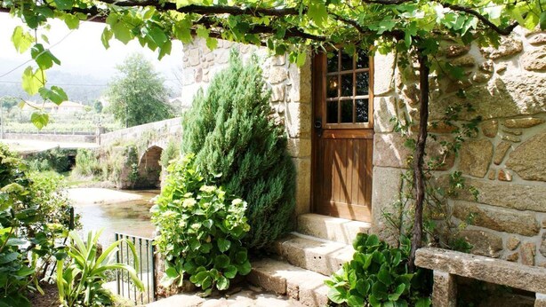 A stone building with a wooden door, steps leading up to it, and a garden with various plants and a small pond. - Villa Estora - One Bedroom Villa, Sleeps 2 (Estorãos)
