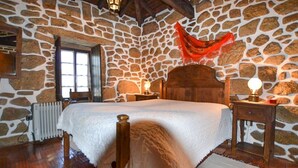A stone-walled bedroom with a wooden bed, a radiator, and a nightstand with a lamp. - Villa Estora - One Bedroom Villa, Sleeps 2 (Estorãos)