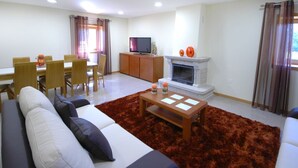 A living room with a sofa, a coffee table, a fireplace, a TV, and a dining area with chairs and a table. - Villa Anabela - Three Bedroom Villa, Sleeps 6 (Povoa de Varzim)