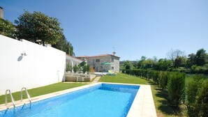 A swimming pool with a white wall, a stone building in the background, and a well-maintained lawn. - Villa Anabela - Three Bedroom Villa, Sleeps 6 (Povoa de Varzim)