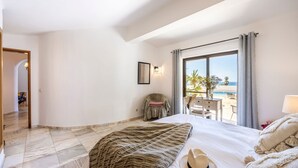 A hotel room with a bed, a chair, a desk, and a view of the beach. - Villa Lua - Three Bedroom Villa, Sleeps 6 (Lagoa)