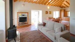 A cozy living room with a sofa, TV, and a wood-burning stove. - Villa Anisa - Four Bedroom Villa, Sleeps 8 (Estorãos)