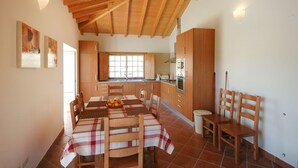 A kitchen with wooden cabinets, a dining table with chairs, and a window. - Villa Anisa - Four Bedroom Villa, Sleeps 8 (Estorãos)