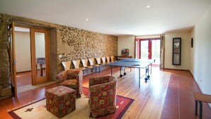 A spacious room with a stone wall, a ping pong table, and several cushioned chairs. - Villa Alexa - Six Bedroom Villa, Sleeps 12 (Fornelos)