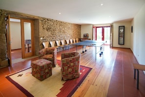 A spacious room with a stone wall, a ping pong table, and several cushioned chairs. - Villa Alexa - Six Bedroom Villa, Sleeps 12 (Fornelos)