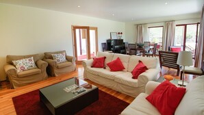 A spacious living room with a beige sofa set, a black coffee table, and red cushions. There is a dining area with a table and chairs, and a piano in the background. - Villa Alexa - Six Bedroom Villa, Sleeps 12 (Fornelos)