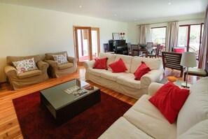 A spacious living room with a beige sofa set, a black coffee table, and red cushions. There is a dining area with a table and chairs, and a piano in the background. - Villa Alexa - Six Bedroom Villa, Sleeps 12 (Fornelos)