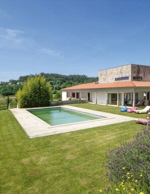 Ein modernes Haus mit Swimmingpool, einer Terrasse mit Liegestühlen und einem Garten.