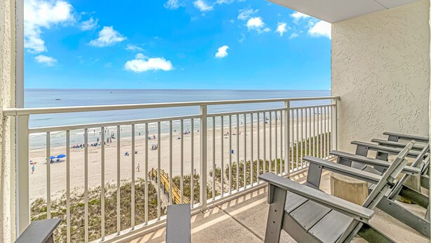 A balcony with a view of a beach, a railing, and a concrete wall.