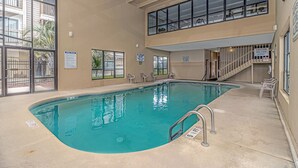 An indoor swimming pool with clear pool rules and no lifeguard on duty signs, surrounded by windows and chairs.