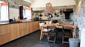 A kitchen with a stone wall, wooden cabinets, a wooden dining table, and a hanging pot rack. - Villa Ava - Four Bedroom Villa, Sleeps 8 (Refóios do Lima)