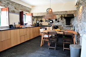 Une cuisine avec un mur en pierre, des placards en bois, une table à manger en bois et un porte-ustensiles suspendu.
