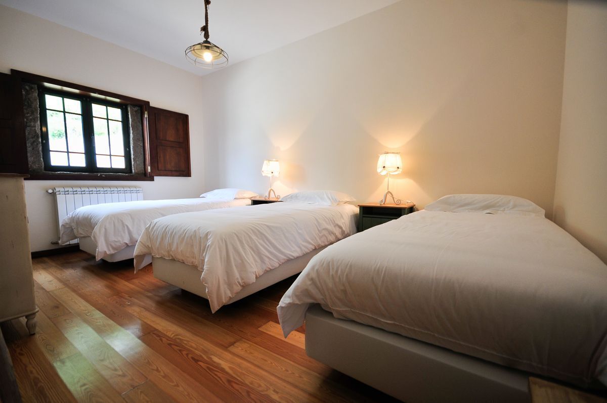 A room with three beds, wooden flooring, a radiator, and a window with shutters.
