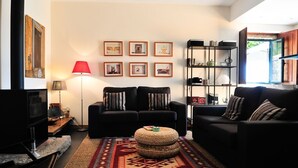A modern living room with two black sofas, a red floor lamp, a woven ottoman, and a bookshelf.
