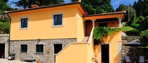 Un bâtiment à deux étages, avec une base en pierre et une partie supérieure de couleur orange, doté de nombreuses fenêtres et d’un espace extérieur couvert aménagé avec des chaises.