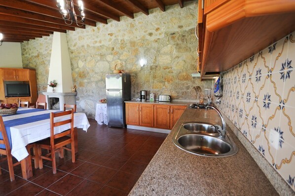 A rustic kitchen with stone walls, wooden cabinets, a granite countertop, and a dining area with a table and chairs.