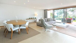 A modern living room with a round dining table, grey sofa, and a large sliding glass door leading to an outdoor area. - Villa Senande - Five Bedroom Villa, Sleeps 10 (Âncora)