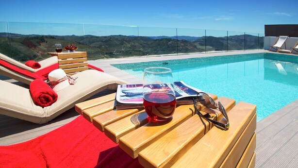 Ein Poolbereich mit Liegestühlen, einem Holztisch mit einem Glas Rotwein und einer Zeitschrift.