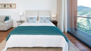 Ein Schlafzimmer mit einem großen Bett, einem Sofa, einem Nachttisch und Blick auf eine gebirgige Landschaft.