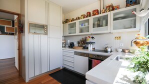 A modern kitchen with white cabinetry, a built-in oven, and a sink. There are various kitchen items and decorations on the countertops. - Moradia Moledo - Three Bedroom Villa, Sleeps 6 (Moledo)