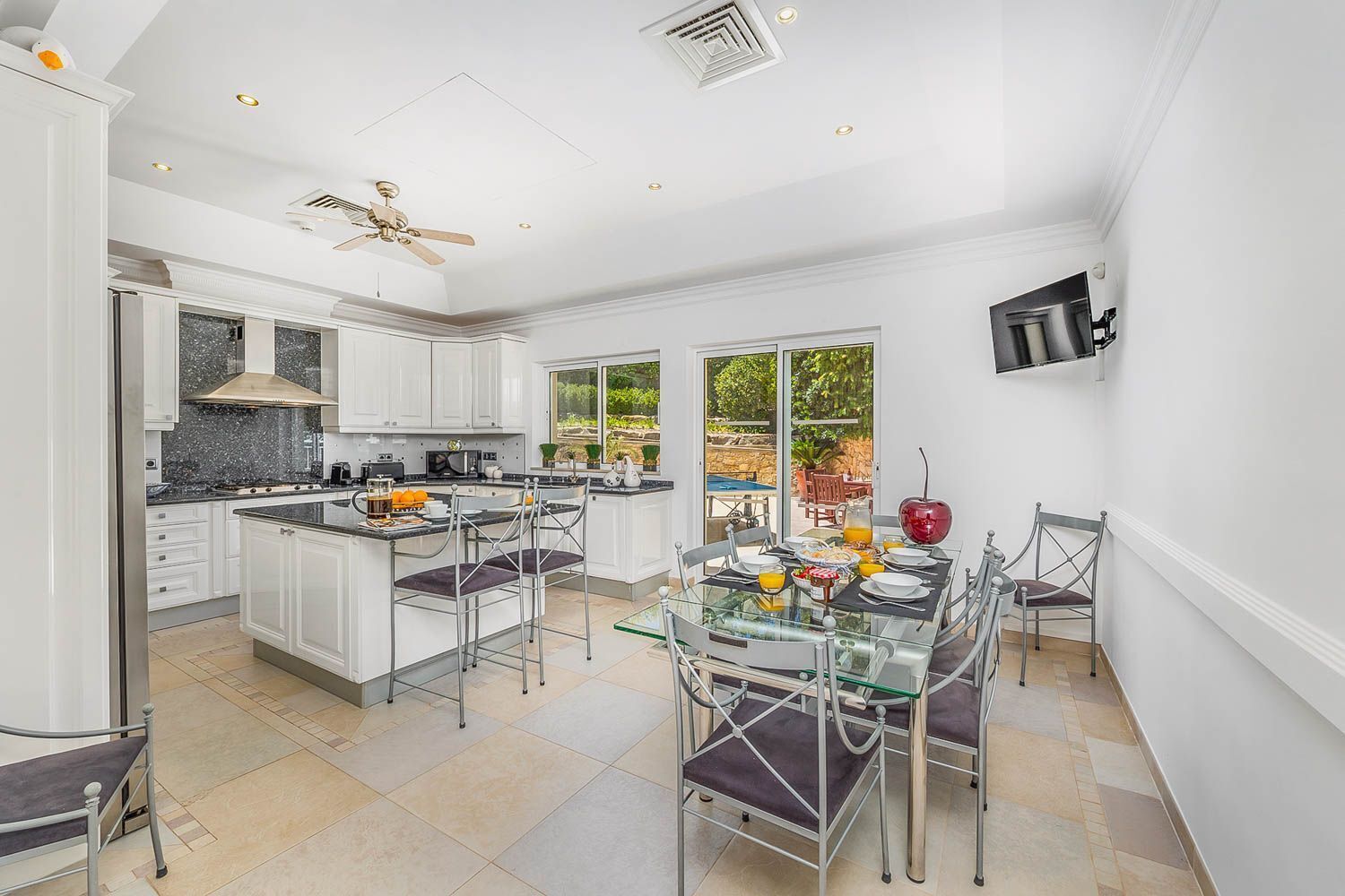 A modern kitchen with white cabinetry, a central island, and a dining area with a glass table and metal chairs.