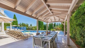 Ett takförsett utomhusområde med plats för att äta, och en pool i bakgrunden.