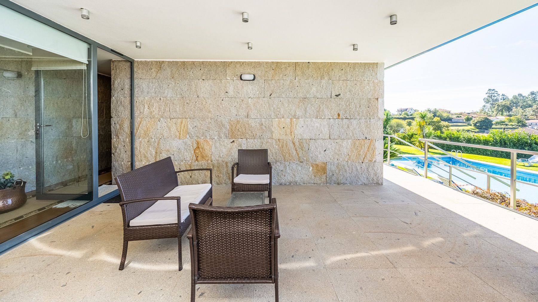 A balcony with wicker furniture, a glass door, and a view of a swimming pool and greenery.