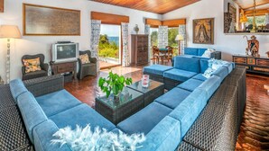 A spacious living area with a large blue sofa, a television, and a dining table with chairs. - Quinta Jordia - Twelve Bedroom Villa, Sleeps 26 (Lagoa)